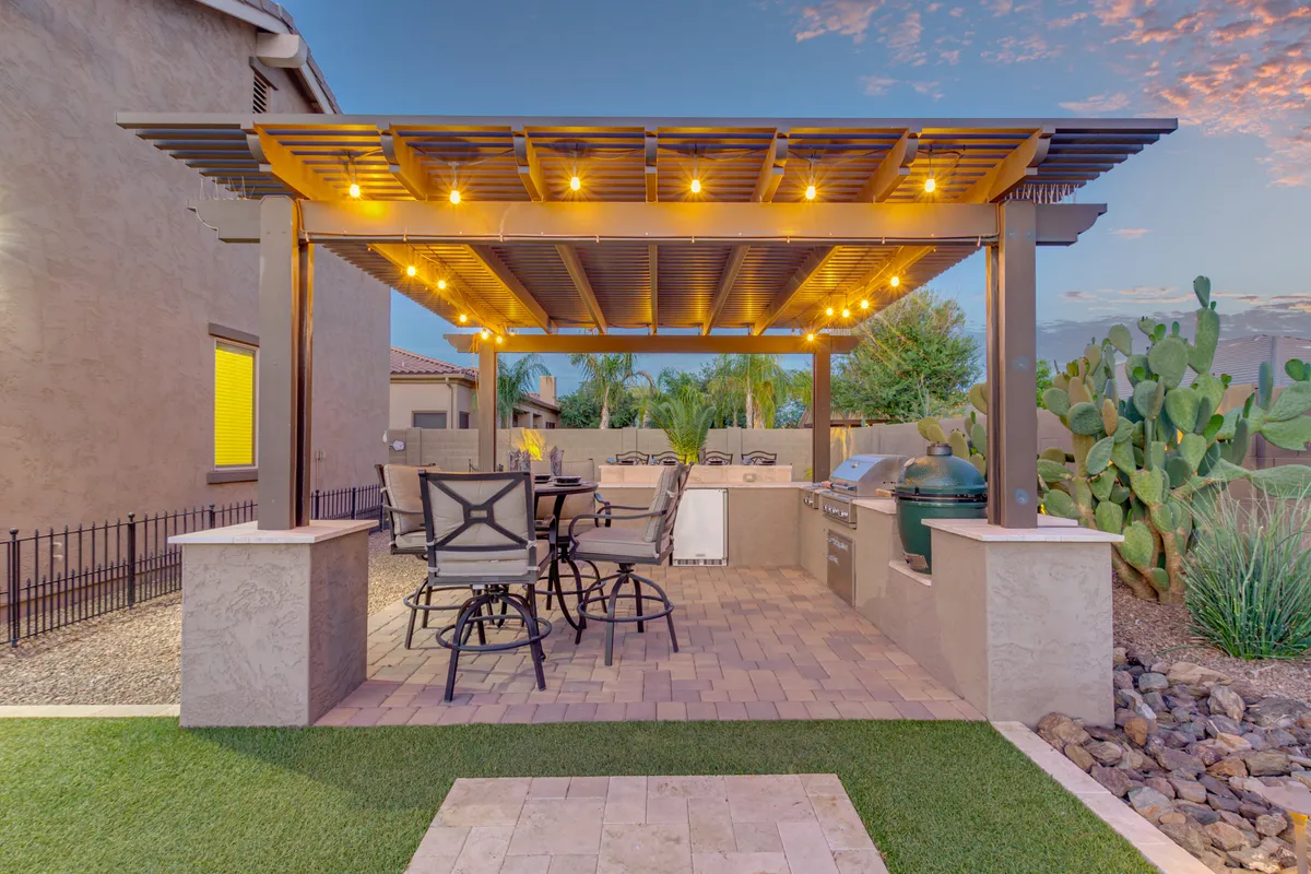 A welcoming pergola area with string lights, an outdoor dining set, a built-in grill station, and signature cactus plants. The space is set for al fresco meals and social gatherings under the Arizona sky.
