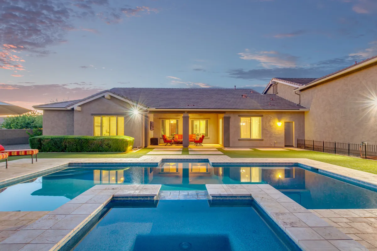 This image captures a tranquil exterior view of the swimming pool surrounded by lush landscaping and an inviting outdoor seating area. The scene is bathed in warm sunset light, creating a relaxing, resort-like atmosphere ideal for wellness and leisure activities such as swimming, lounging, and alfresco dining.