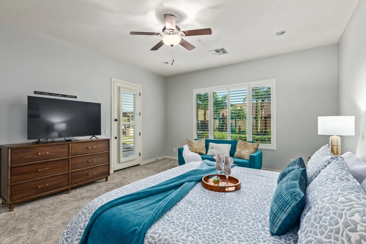 A cozy bedroom with a queen bed adorned by a decorative throw, a television, a window seat perfect for reading or enjoying views, and a wooden dresser. The room exudes warmth and offers personal space for quiet moments.