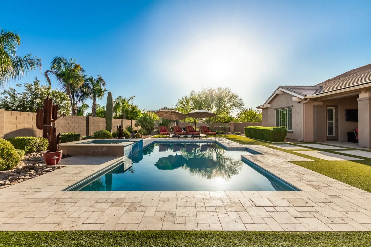 A cheerful backyard scene featuring a glistening swimming pool, patio seating, and lush landscaping. Sunlight dances on the water, creating a lively yet relaxing atmosphere ideal for summer parties, casual mornings, or sunset gatherings with friends and family.
