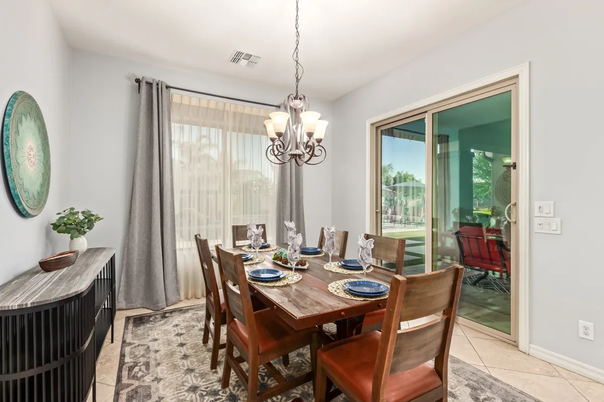 A refined dining room centered around an elegant dining table, illuminated by a stylish chandelier with a window view. The ambiance is warm and welcoming, suited for intimate dinners or celebratory meals.