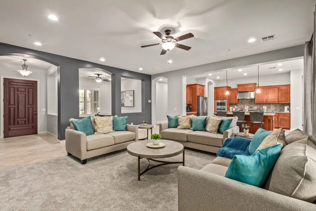A spacious, open-concept living room featuring plush sofas arranged for conversation, a central coffee table, and a clear view of the adjacent kitchen area. Decorative cushions and soft lighting give the room a cozy-yet-elegant feel, making it ideal for both relaxation and social gatherings.