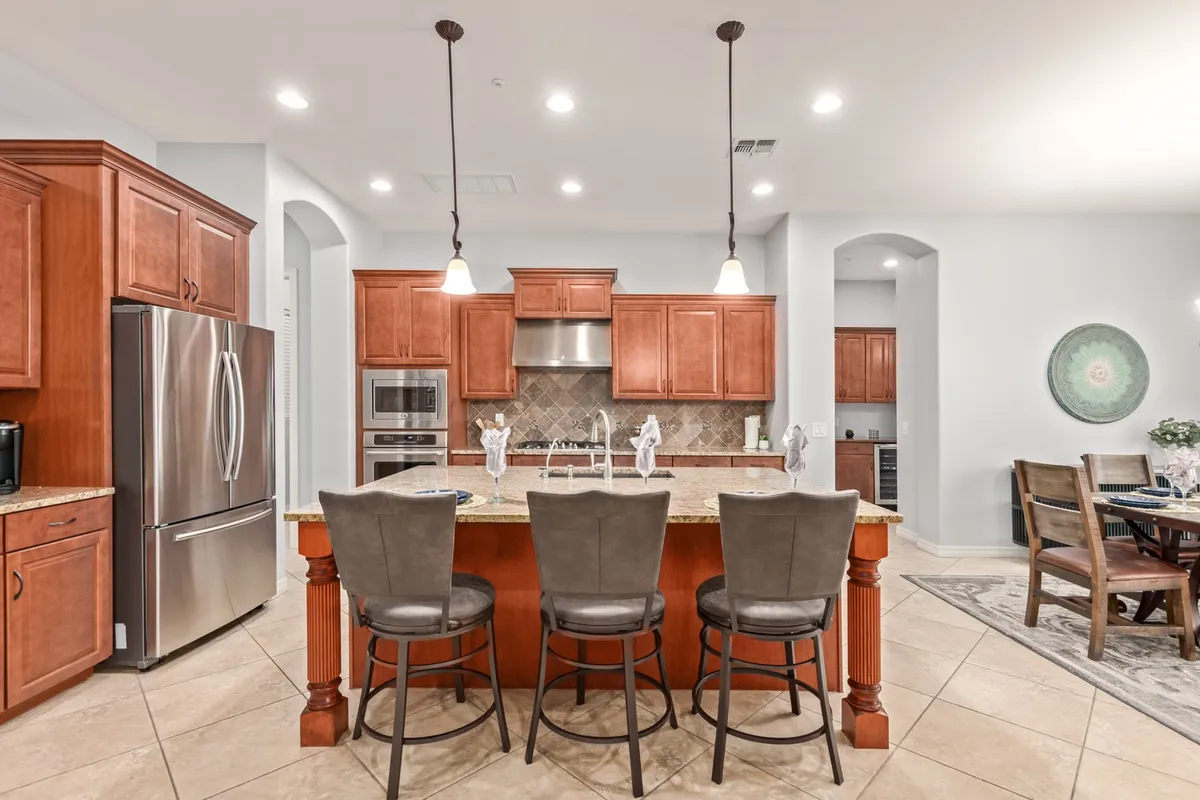 A warm, open kitchen scene featuring a central island, stainless steel appliances, wood cabinetry, and an adjacent dining area. The space is designed for both culinary creativity and friendly gatherings, with high-quality finishes throughout.