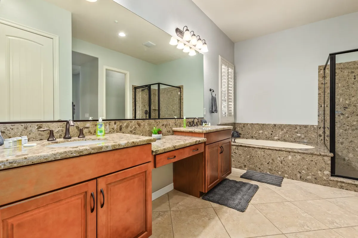 A spa-inspired bathroom showcasing double vanities with sinks, a large shower enclosure, a soaking bathtub, and a mirrored wall. The space is bright, elegant, and designed for relaxation and self-care routines.