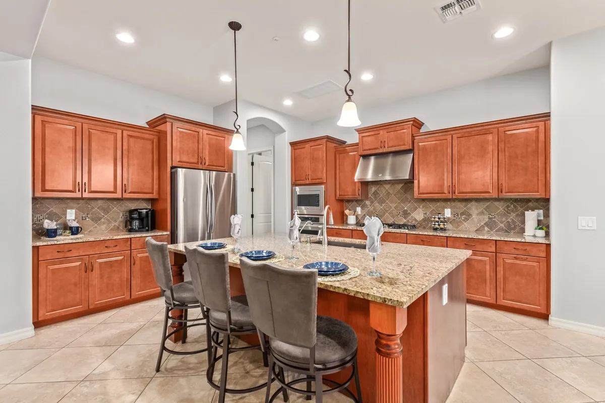 A modern kitchen with an oversized granite island featuring seating, surrounded by warm, wooden cabinets and sleek stainless steel appliances. The area exudes functionality and style, ideal for both daily routines and hosting guests.