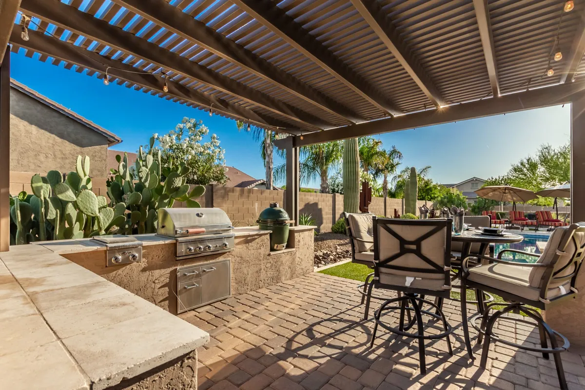 A dynamic view of the outdoor kitchen with built-in BBQ and smoker, adjacent to the swimming pool and comfortable seating area surrounded by lush cacti and greenery. The space feels perfect for entertaining, from afternoon barbecues to quiet poolside mornings.