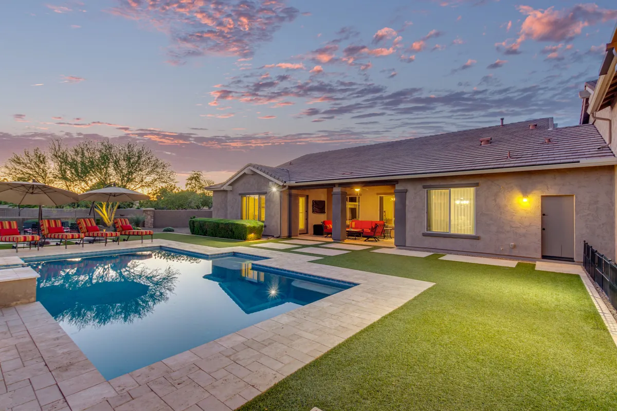 A serene backyard scene featuring a sparkling swimming pool, a comfortable outdoor seating area with plush chairs, and a beautifully landscaped garden. The space is clearly designed for both relaxation and entertaining, with plenty of room for lounging and enjoying the outdoors.