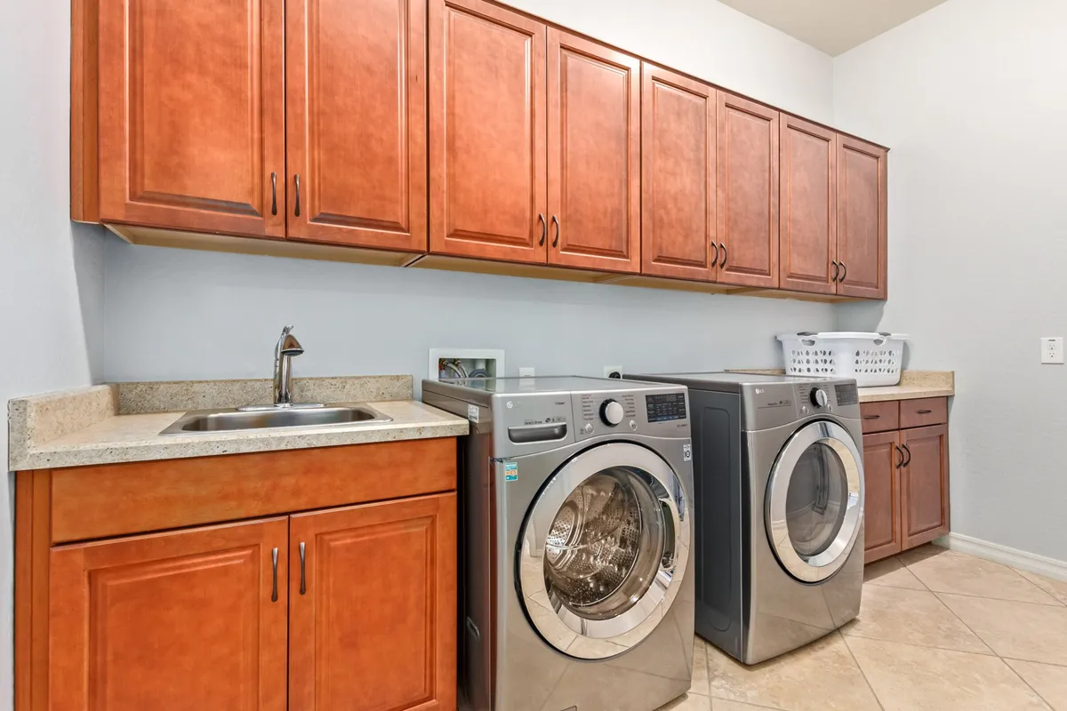 A modern laundry room featuring a washer and dryer, sink, and plentiful storage cabinets. The space looks clean, organized, and highly functional, supporting the needs of long-term guests and families.